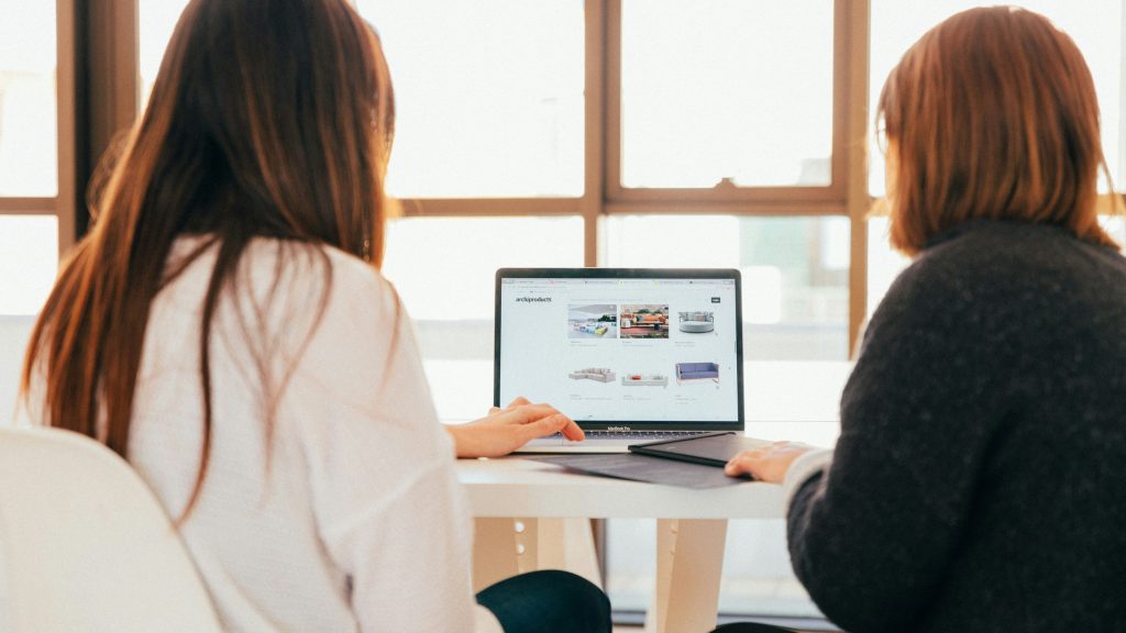 Two professional women looking at a website on a laptop in a bright office.
