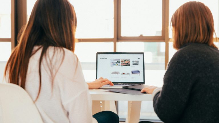 Two professional women looking at a website on a laptop in a bright office.