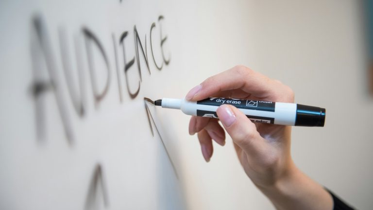 Hand writing "audience" on a whiteboard with a dry erase marker.